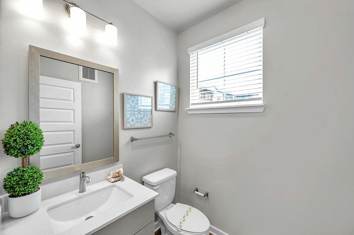 Bright, modern bathroom with sleek fixtures, large mirror, and natural light from window blinds.