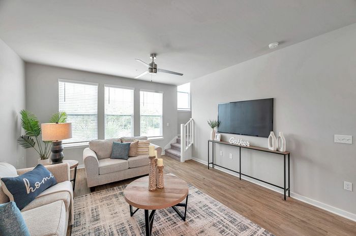 Inviting living room with modern d&eacute;cor, featuring a cozy sofa, stylish round coffee table, and sleek entertainment console, bathed in abundant natural light from large windows.