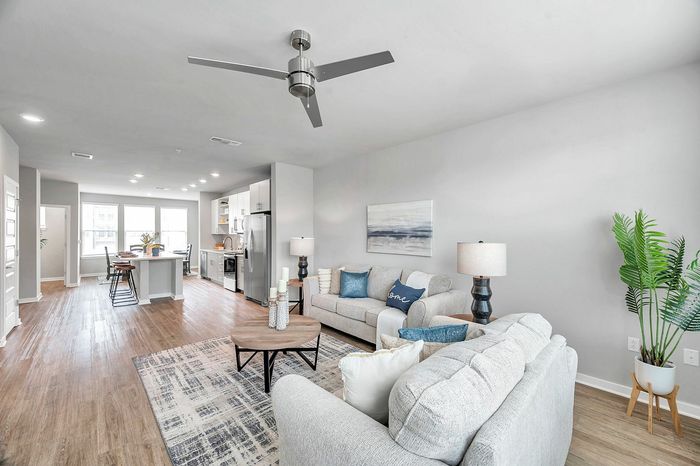 Bright, modern open-concept living room and kitchen with stylish decor, featuring cozy sofas, chic dining area, and vibrant greenery.