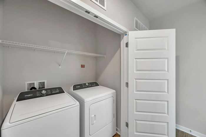 Modern laundry area with sleek Whirlpool washer and dryer, featuring convenient shelving and elegant white door for space efficiency.