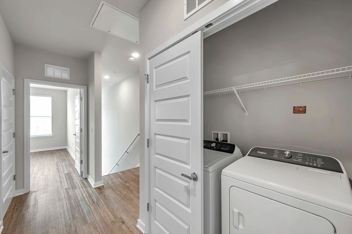 Bright hallway with elegant wood flooring leading to a cozy laundry area featuring modern washer and dryer units.