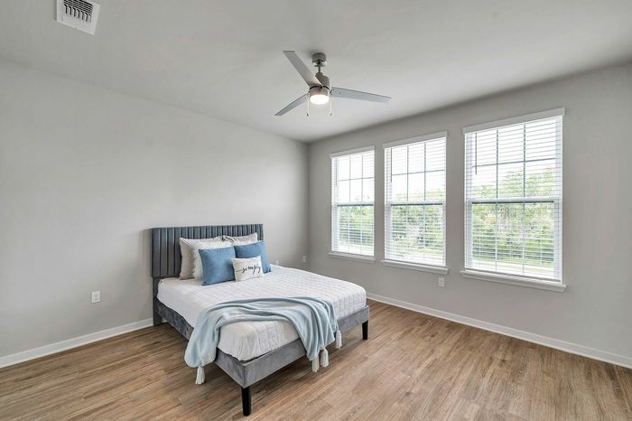 Bright and inviting bedroom with modern ceiling fan, large windows, and elegant wood flooring, perfect for relaxation.