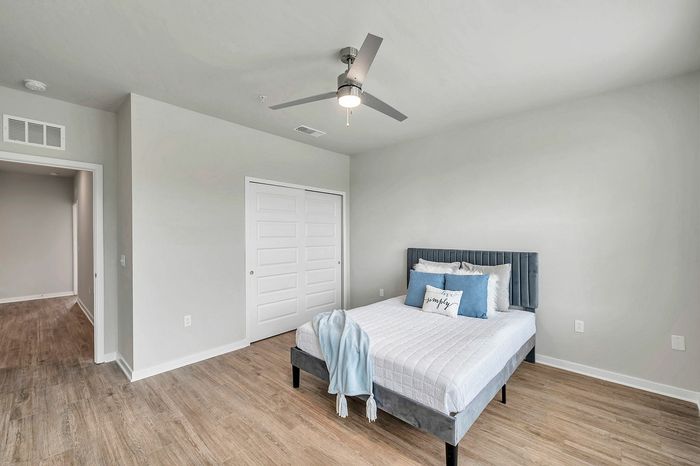 Bright and airy bedroom with sleek wood flooring, modern ceiling fan, and stylish double closet doors.
