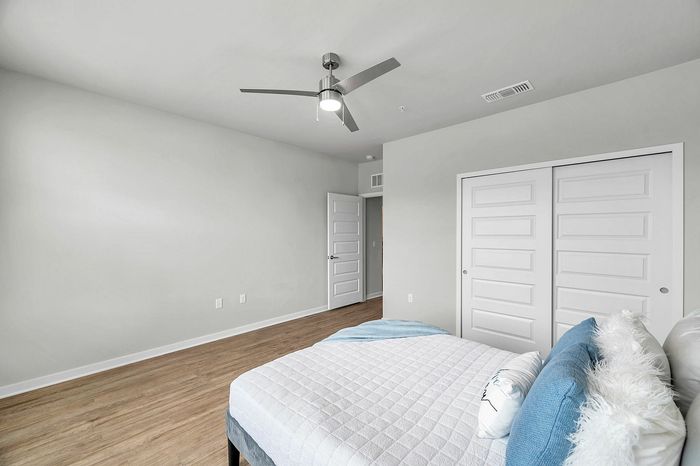 Modern bedroom with sleek ceiling fan and ample natural light, featuring stylish doors and a plush bed.