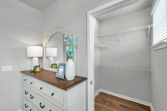 Elegant bedroom corner featuring a vintage-style dresser with a decorative mirror, soft lighting, and a spacious walk-in closet with natural light.