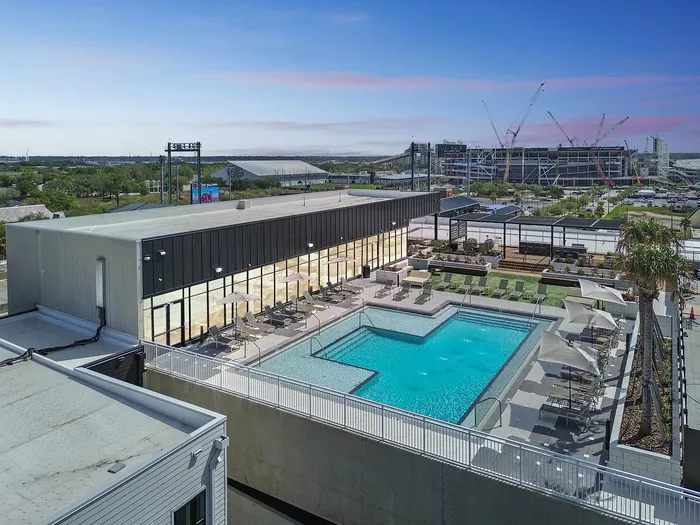 Modern apartment complex featuring a luxurious outdoor swimming pool with sun loungers and a spacious deck, set against an urban skyline.