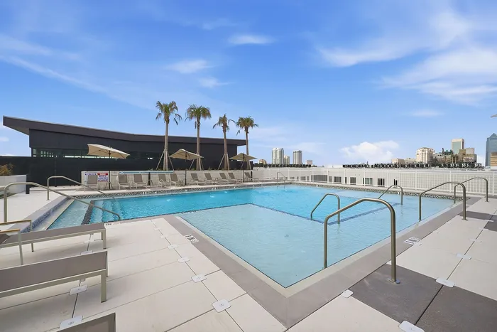 Luxurious rooftop pool with sleek loungers, tall palm trees, and a stunning city skyline backdrop.