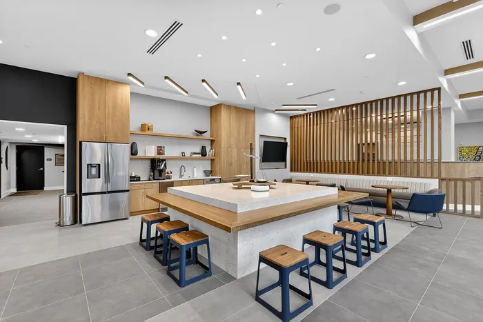 Modern communal kitchen with sleek wooden cabinetry, a central island with seating, stainless steel appliances, and a cozy seating area.