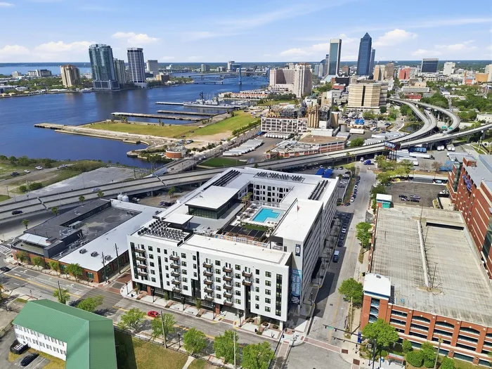 Modern cityscape with a luxurious apartment complex featuring a rooftop pool, nestled by the waterfront with stunning urban and river views.