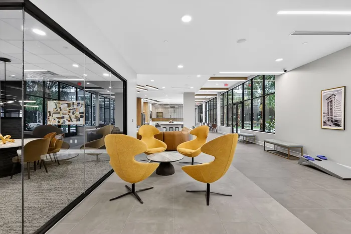 Modern communal lounge with vibrant yellow chairs, sleek glass walls, and panoramic windows offering abundant natural light.