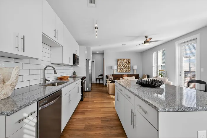Elegant open-concept kitchen with sleek white cabinetry, granite countertops, and views into a sunlit living area adorned with modern decor.