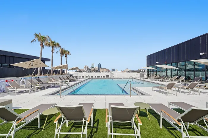 Luxurious rooftop pool with sun loungers, palm trees, and stunning city skyline views.