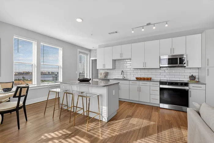Modern kitchen with sleek white cabinets, an elegant island with chic bar stools, and sunlit dining area showcasing expansive city views through large windows.