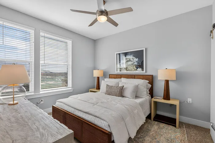 Inviting bedroom with stylish decor, featuring a cozy bed, modern ceiling fan, and ample natural light from large windows.