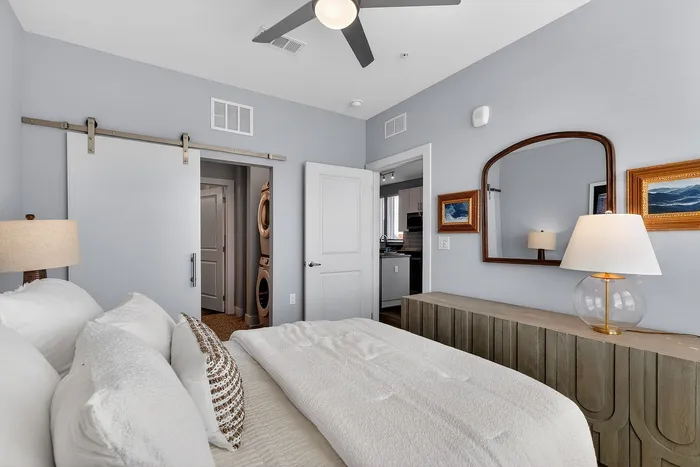 Bright and modern bedroom featuring a cozy bed, stylish sliding barn door, and elegant decor with a glimpse into the kitchen and laundry area.