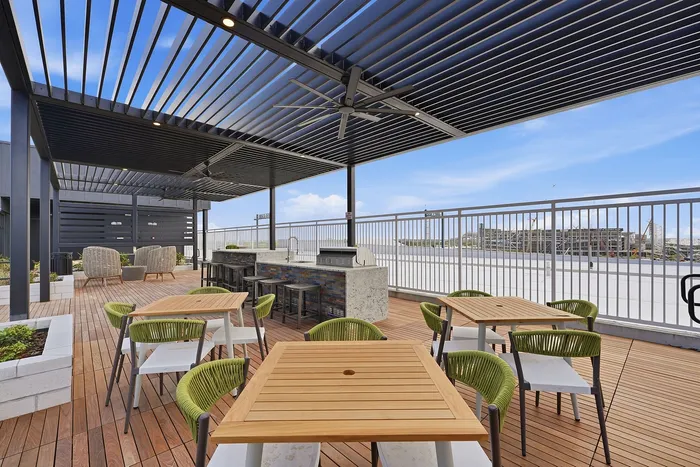 Elegant outdoor terrace with modern pergola, featuring stylish wooden tables and vibrant green chairs, offering a perfect space for al fresco dining and relaxation.