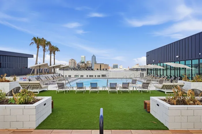 Luxurious rooftop sundeck with swimming pool, sun loungers, and panoramic city views set against a vibrant blue sky.