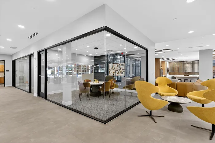 Modern office space featuring elegant glass-walled conference room and stylish yellow lounge chairs.