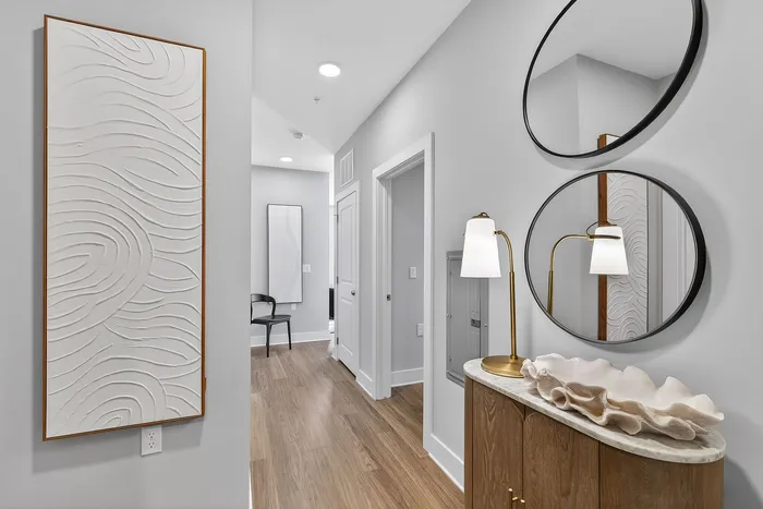 Elegant apartment hallway featuring stylish wooden flooring, modern round mirrors, and artistic wall decor, creating a warm and inviting entrance.