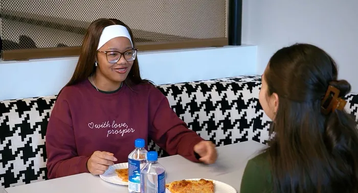 Charming dining area with modern houndstooth patterned seating, featuring two friends enjoying a casual pizza meal and engaging conversation.