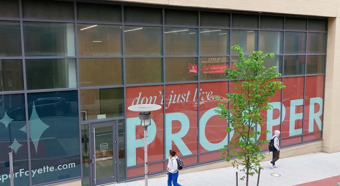 Vibrant city street view with modern building featuring bold 'don't just live, PROSPER' signage, inviting passersby to explore luxurious living opportunities.