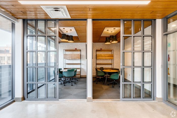 Contemporary office space featuring glass sliding doors, sleek wooden shelves, and modern lighting with round tables and green chairs.