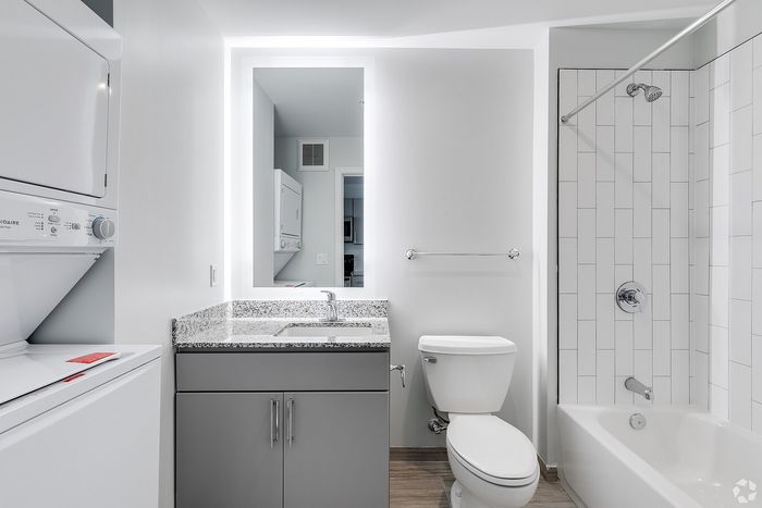 Modern bathroom with sleek granite countertop, integrated washer and dryer, and a stylish tile bath.