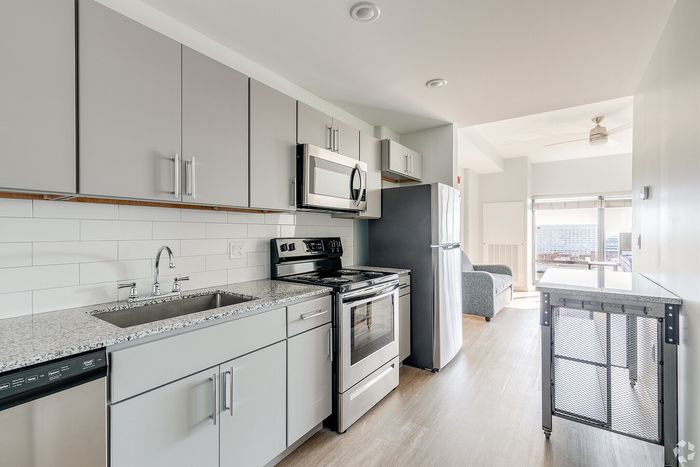 Chic modern kitchen with sleek gray cabinets, stainless steel appliances, and a bright open layout leading to a sunlit living area with expansive city views.