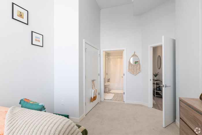 Bright and airy bedroom featuring soft beige carpeting, minimalist decor, and modern ensuite bathroom with stylish white tiles.