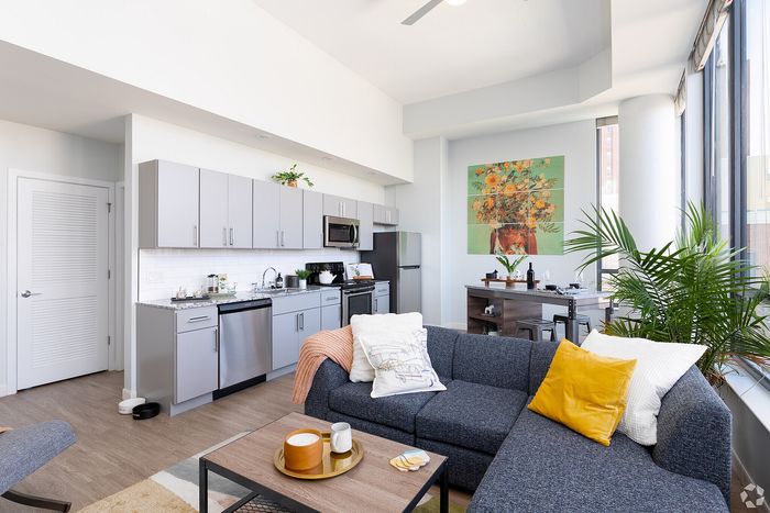 Modern living space featuring an elegant kitchen with gray cabinets, a cozy blue sectional sofa, and large windows letting in abundant natural light.