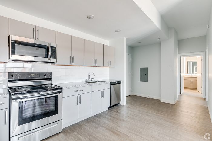 Modern kitchen with stainless steel appliances, sleek cabinetry, and hardwood flooring leading to a bright bathroom.