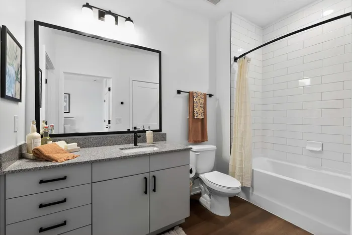 Elegant bathroom with a sleek granite countertop, large mirror, and stylish white tiled shower.