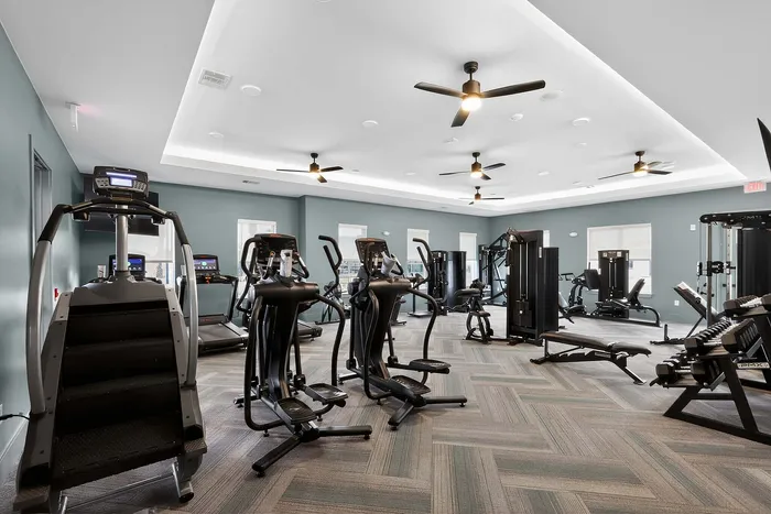 Modern fitness center with state-of-the-art exercise equipment, featuring treadmills, ellipticals, and strength training machines in a spacious, well-lit room.