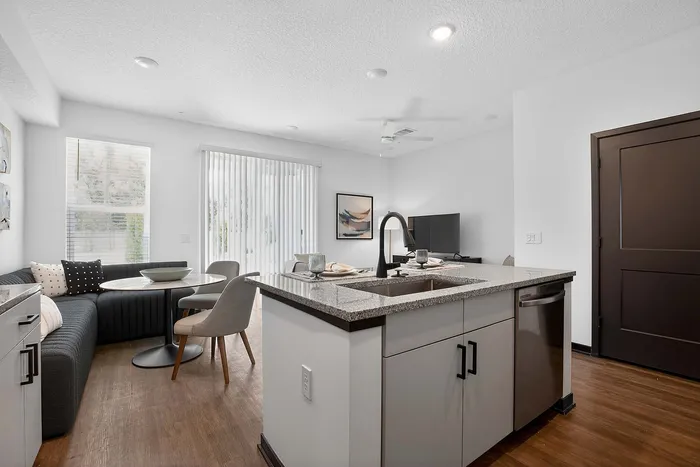 Inviting modern apartment kitchen and dining area with an elegant island, stylish gray sofa, and bright natural light filtering through large windows.