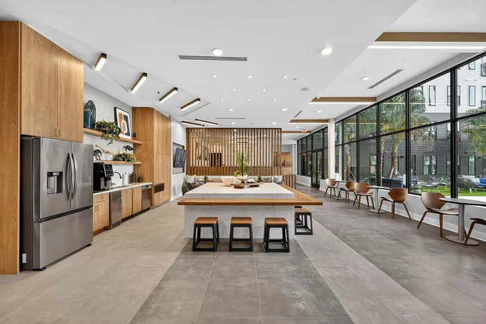 Modern community lounge featuring a sleek kitchen area, spacious seating, and panoramic windows with outdoor views.