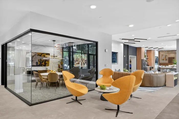 Modern lobby area featuring elegant yellow chairs, a stylish glass-enclosed meeting room, and a cozy seating area with a contemporary design.
