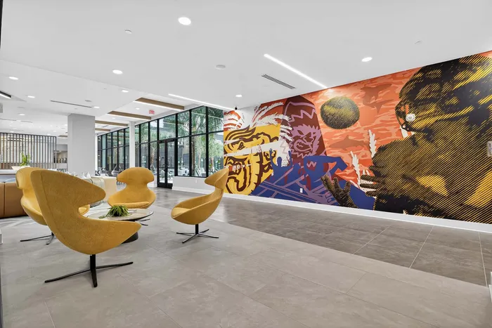 Contemporary lobby featuring sleek mustard-yellow chairs, expansive glass windows, and a vibrant artistic mural.