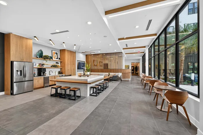 Elegant communal kitchen and lounge area featuring sleek stainless steel appliances, a central island with stylish seating, and floor-to-ceiling windows offering natural light.
