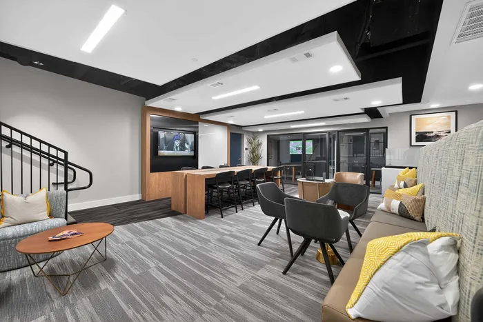 Modern communal lounge area with stylish seating, a sleek wooden table, wall-mounted TV, and contemporary decor, creating an inviting atmosphere.