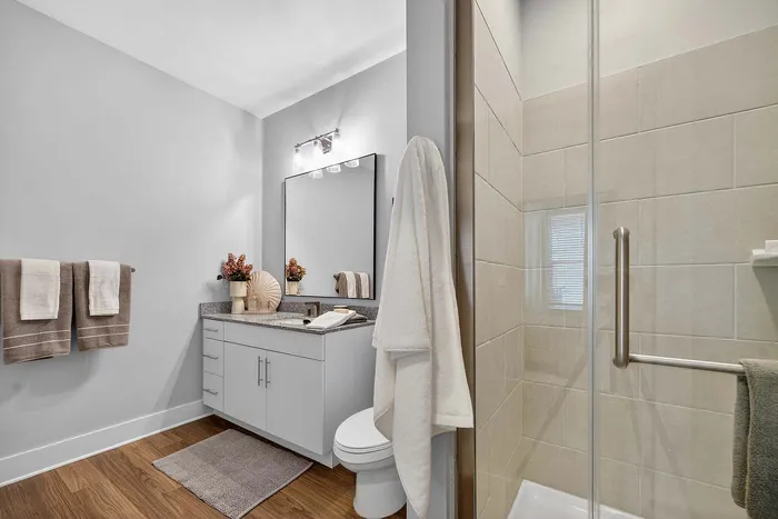 Elegant modern bathroom featuring a sleek vanity with granite countertop, large mirror, and a glass-enclosed shower with beige tiles.