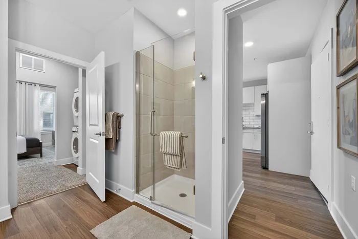 Modern apartment interior featuring a sleek shower, in-unit laundry, and a glimpse of the stylish kitchen with white cabinetry.