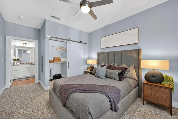 Inviting bedroom with a plush bed, stylish decor, and a spacious walk-in closet leading to a chic bathroom, bathed in natural light.