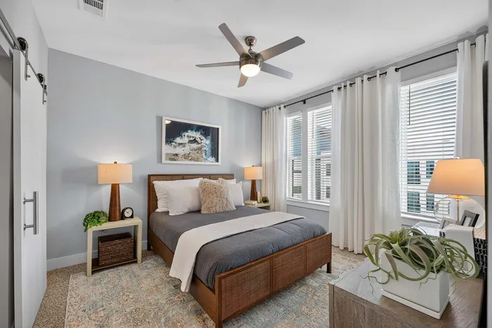 Charming bedroom with elegant decor, featuring a cozy bed, stylish lamps, and large windows with sheer curtains for natural light.