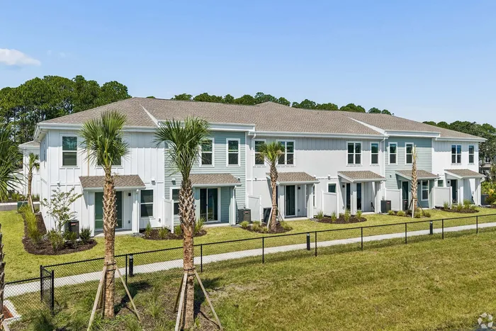 Charming modern townhomes with white and blue exterior, surrounded by lush greenery and palm trees.