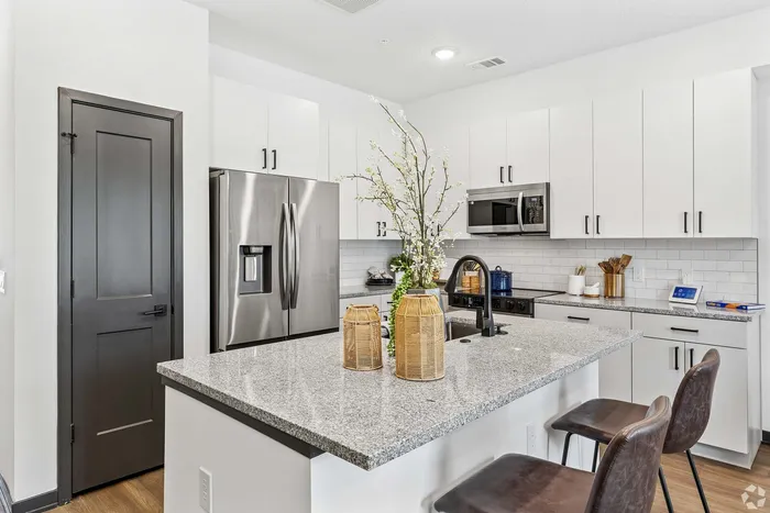Modern kitchen with sleek stainless steel appliances, elegant white cabinetry, and a spacious granite countertop island featuring stylish decor, ideal for cooking and entertaining.