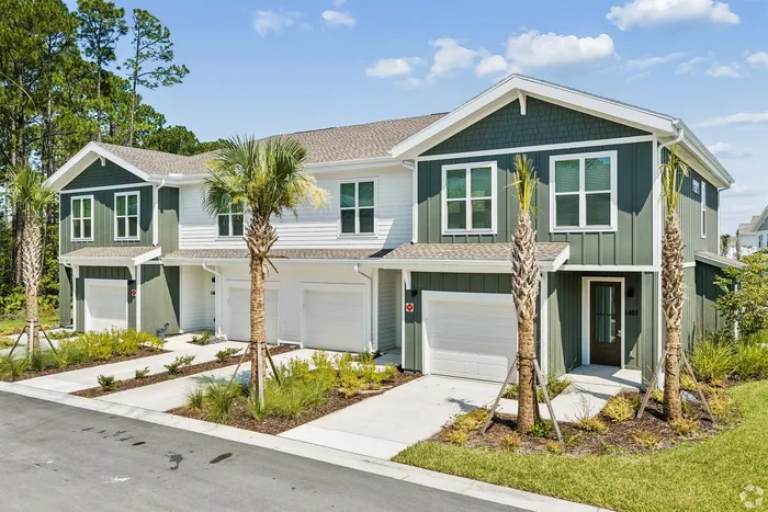 Charming duplex townhouse with a modern facade and lush landscaping, highlighted by tall palm trees and pristine white garages, set against a backdrop of vibrant blue skies.