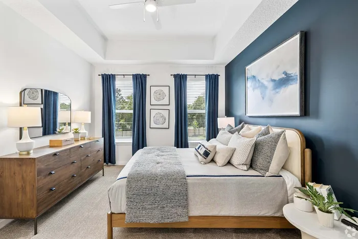 Bright and inviting bedroom with elegant blue accent wall, modern wood dresser, and plush bedding, creating a serene retreat.