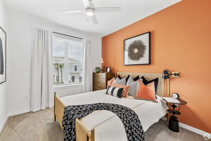 Cozy and modern bedroom with vibrant orange accent wall, elegant decor, and abundant natural light.