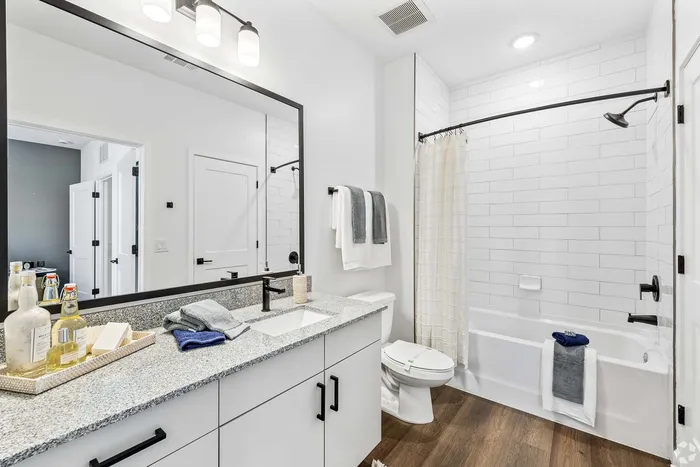 Modern bathroom with sleek granite countertop, white cabinetry, and elegant black fixtures, featuring a spacious shower-tub combo and elegant lighting.
