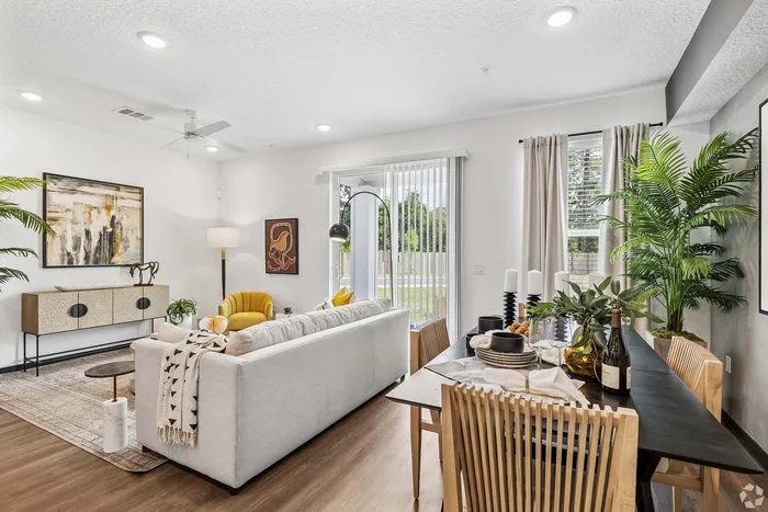 Modern living and dining area with stylish decor, featuring a cozy yellow armchair, elegant artwork, and abundant natural light from large windows.